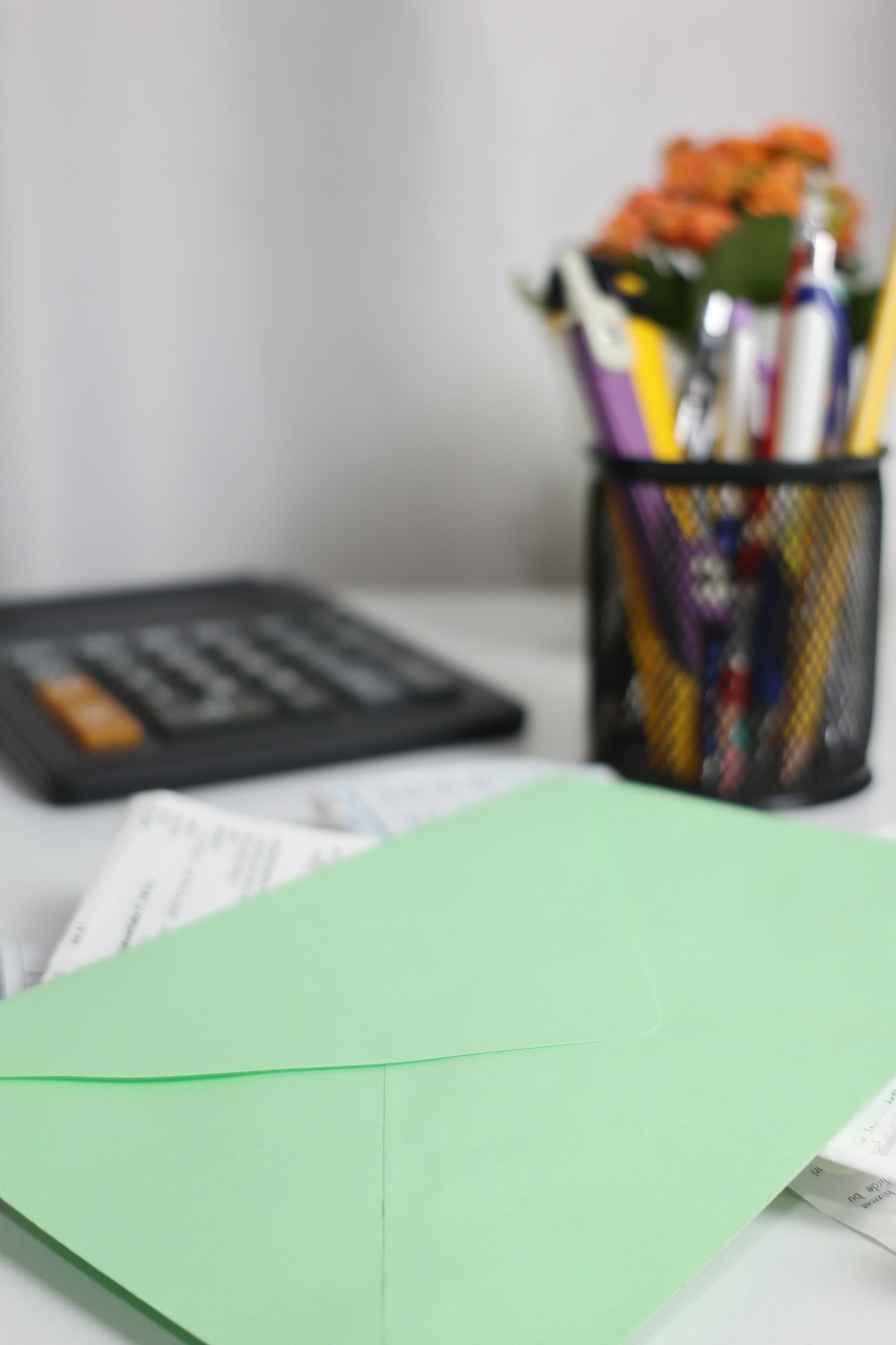 A stack of paper statements and unopened envelopes on a desk beside a pen.