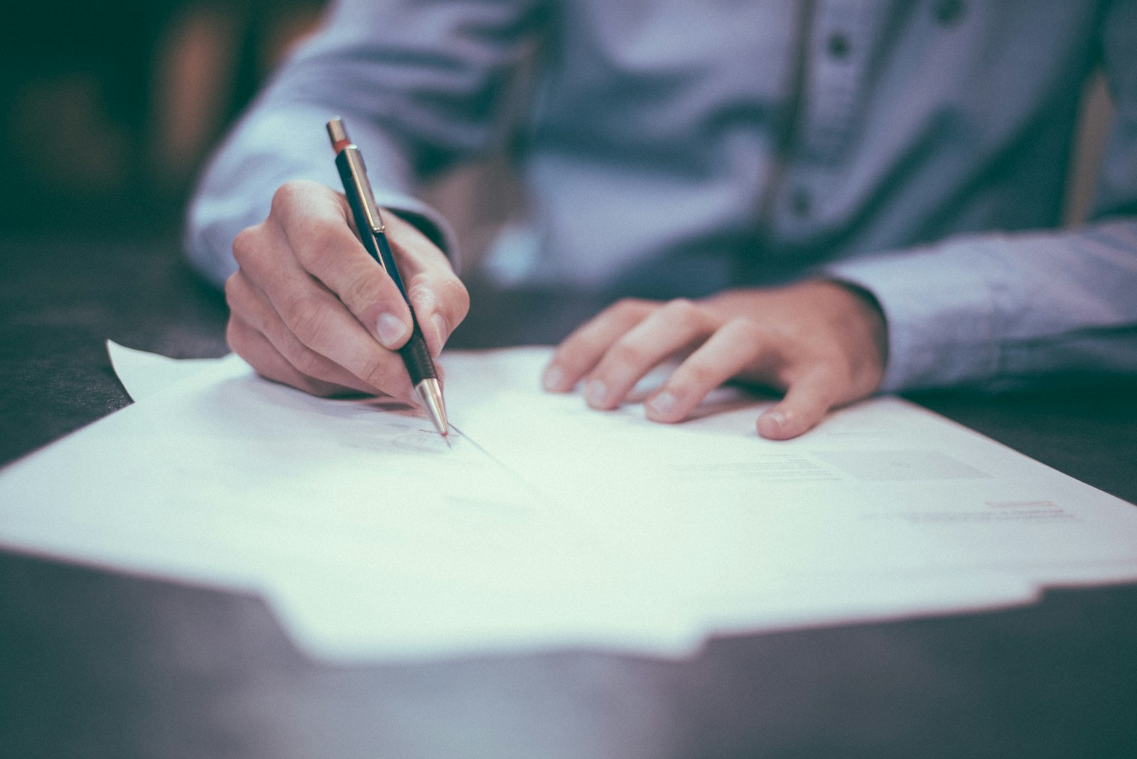 A hand holding a pen over printed pages on a desk.