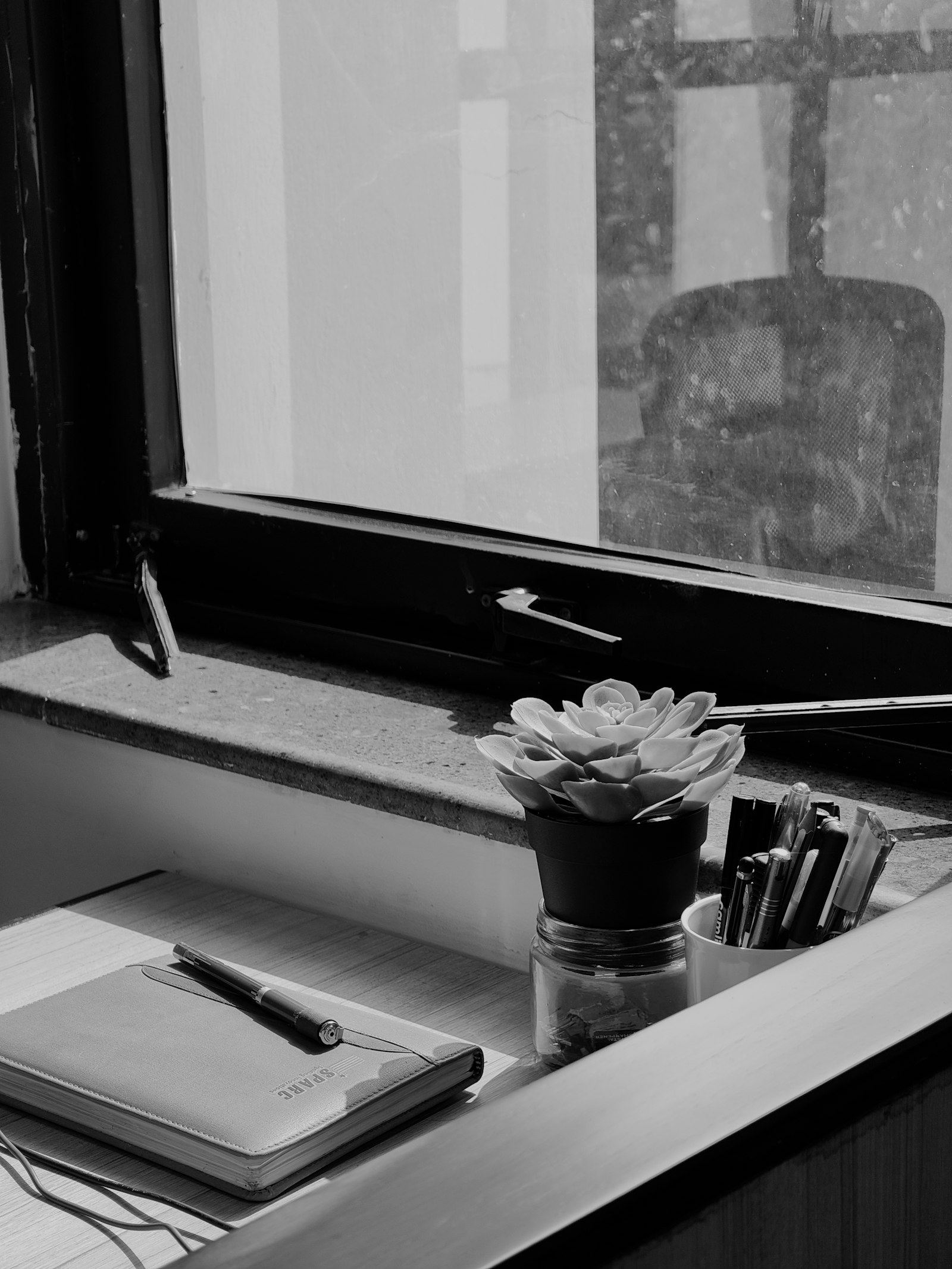 A phone and an open notebook on a desk near a window in soft morning light, set up for taking notes on a call.